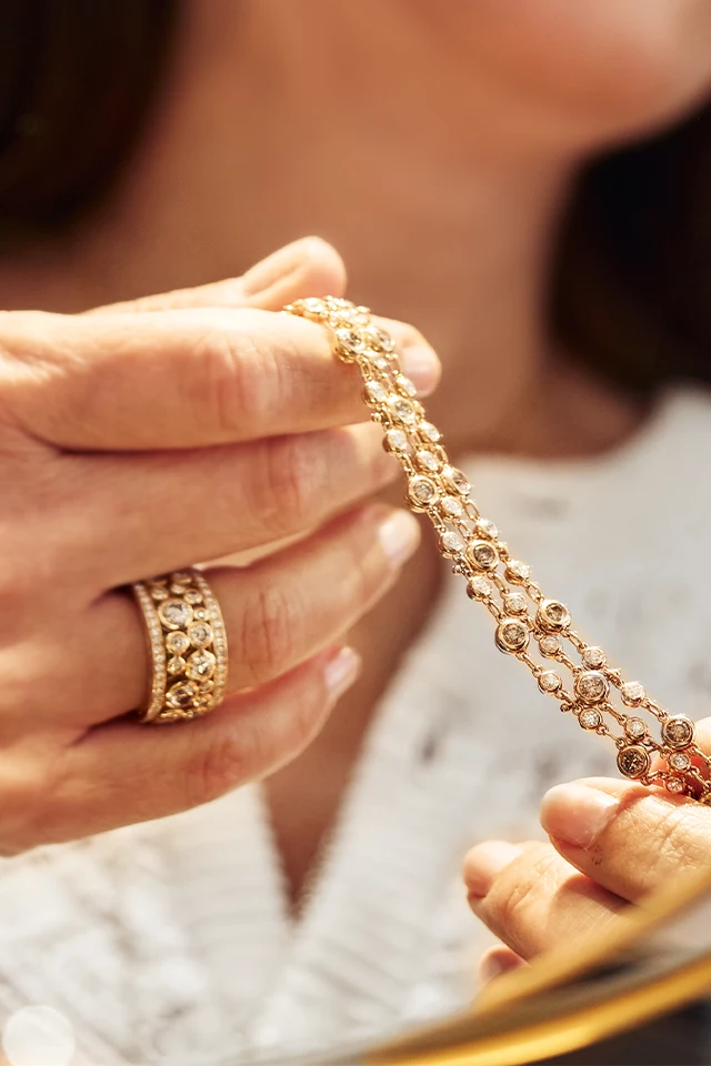 Lächelnde Frau mit Brilliantring hält Kette in den Händen.